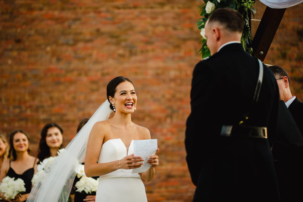 Wedding and Event Destination Bride, medical surgeon, saying her vows to her Groom, in military, during their downtown waterfront Ceremony on the green at Palafox Wharf Waterfront Event and wedding Venue