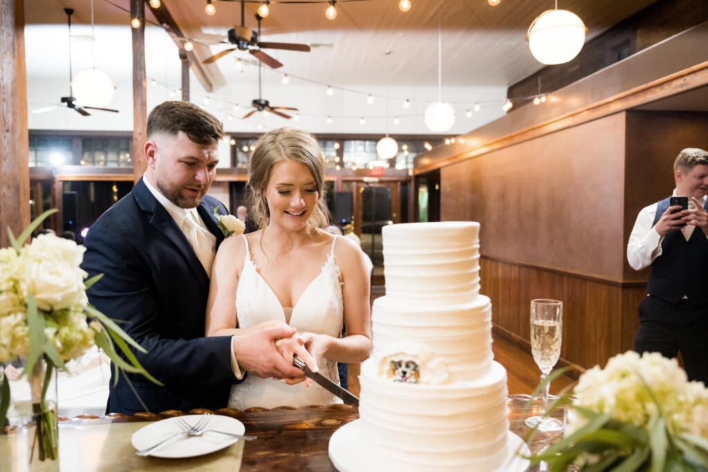 Couple cutting their wedding cake featuring an adorable dog figurine inside Palafox Wharf Waterfront venue . Photo by Aislinn Kate Photography https://www.barnatcedargrove.com/ http://www.vineyardatstcharles.com/
