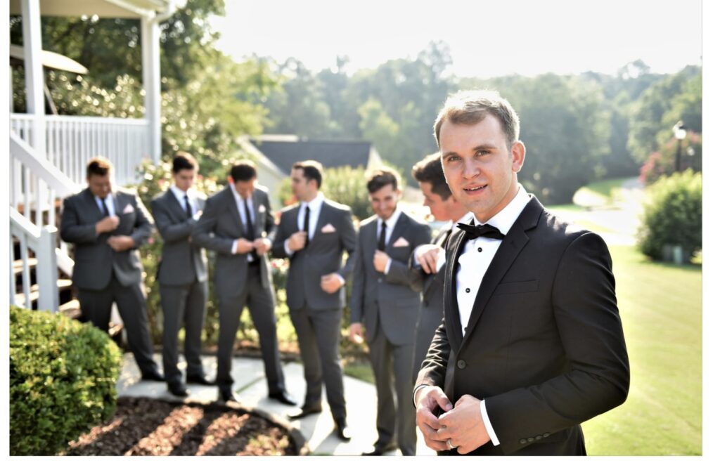 Groom and his Groomsmen in the Background with a green lawn in the background https://617palafoxwharf.com/ https://legacyfarmstn.com/

