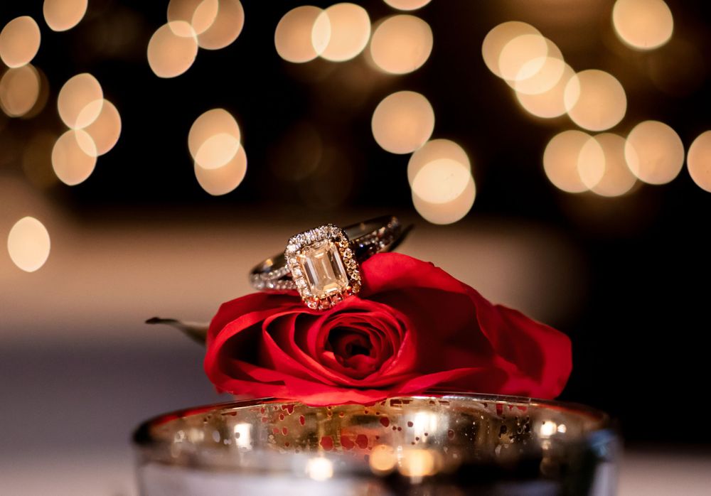 Couple’s rings with red rose and cafe lighting overhead at Palafox Wharf Waterfront.  Photo by Luna Maya Photography Near Pensacola and near Destin Florida
