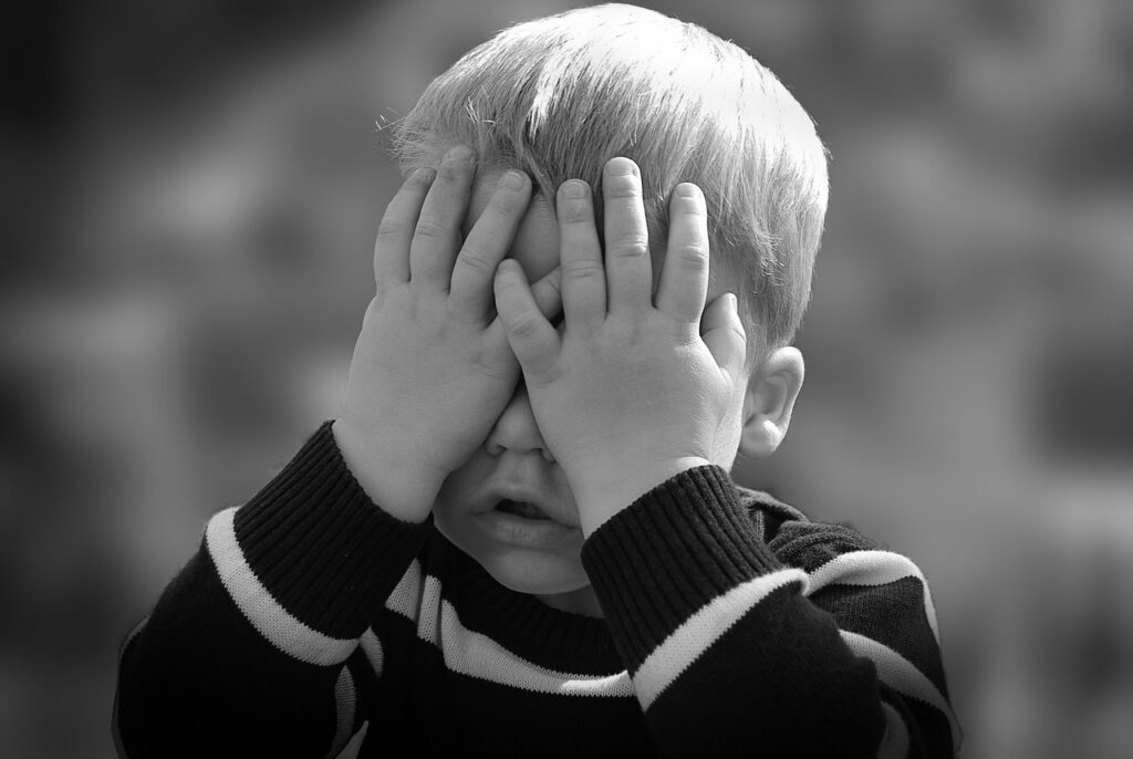 Black and white photo of blond hair boy with his hands over his eyes dressed in a back and white sweater. https://www.1908grand.com/  http://www.thebarnattwiggys.com/