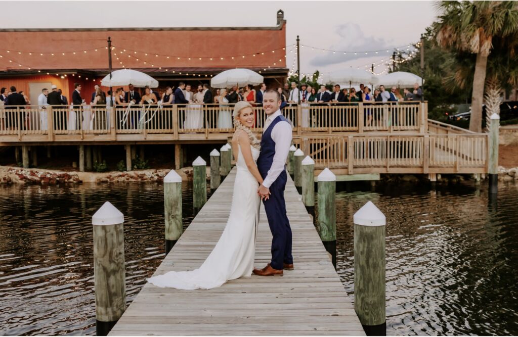 Just Married Couple on Dock Centrally located in Downtown Pensacola showing guests on deck during cocktail hour with cafe lighting overhead and umbrellas with tassels near Destin near Pensacola