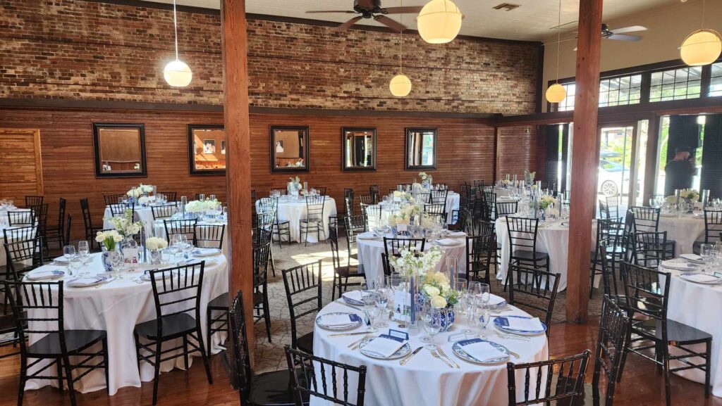 Inside Palafox Wharf Waterfront showing Dining Area with blue and white plate setting, white florals, exposed brick wall with high ceilings near Pensacola Florida near Desting