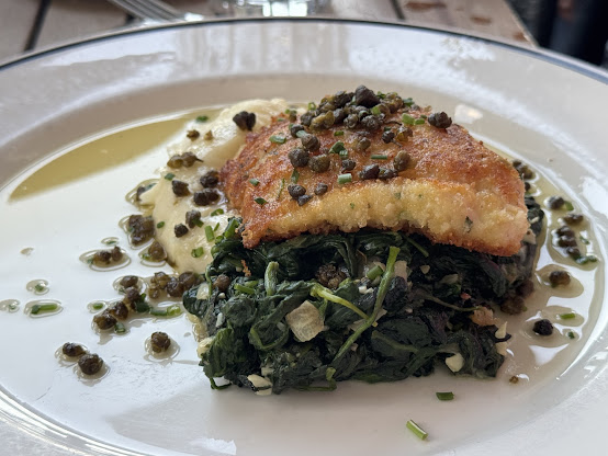 Crispy breaded fish on sautéed spinach with creamy sauce and capers, perfect date ideas in Pensacola.