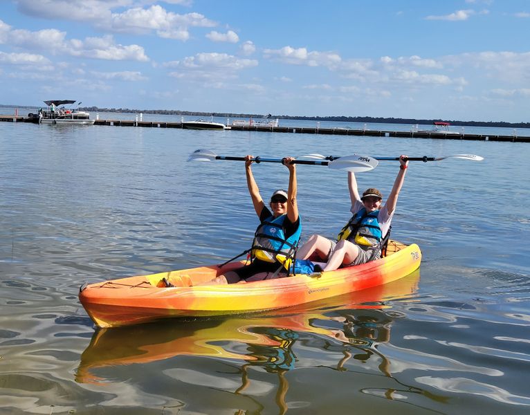 Couple kayaking on calm water with raised paddles, great thing to do after viewing Pensacola wedding venues.