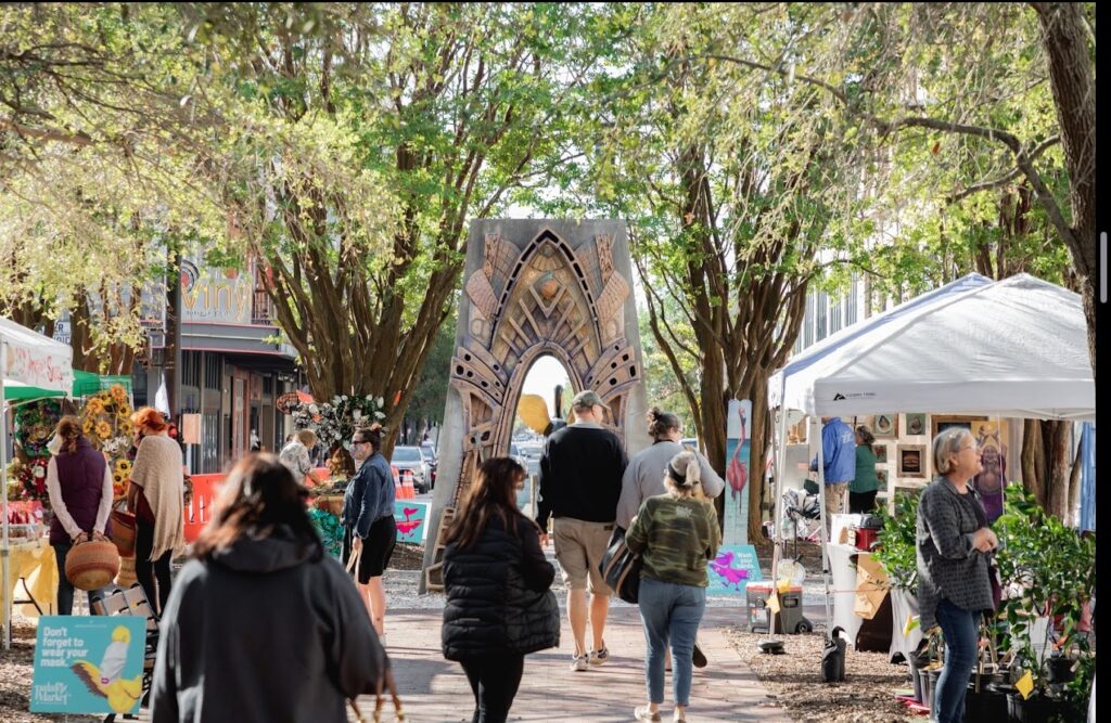 A lively outdoor market with a decorative arch, surrounded by trees and stalls, near wedding venues, ideal for a scenic event or shopping day.