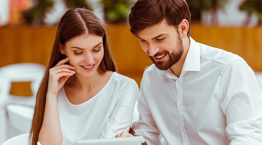 Dating couple in a coffee shop looking at a Ipad.  She has long brown straight hair and both are dressed in white shirts.  http://www.butterflykissespavilion.com/ https://617palafoxwharf.com/