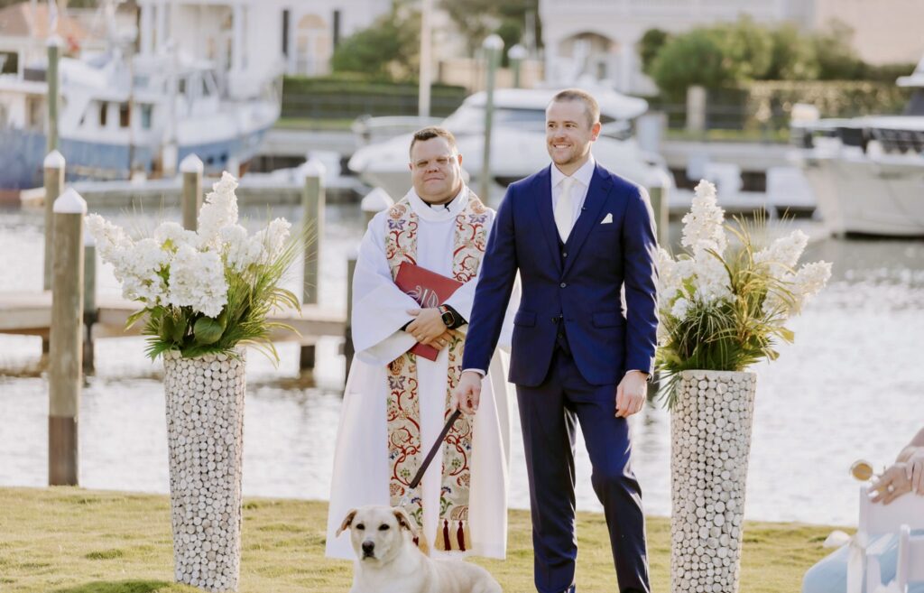 Groom with white doggie and minister in the background on the Palafox Wharf Waterfront at Ceremony on the Green Lawn