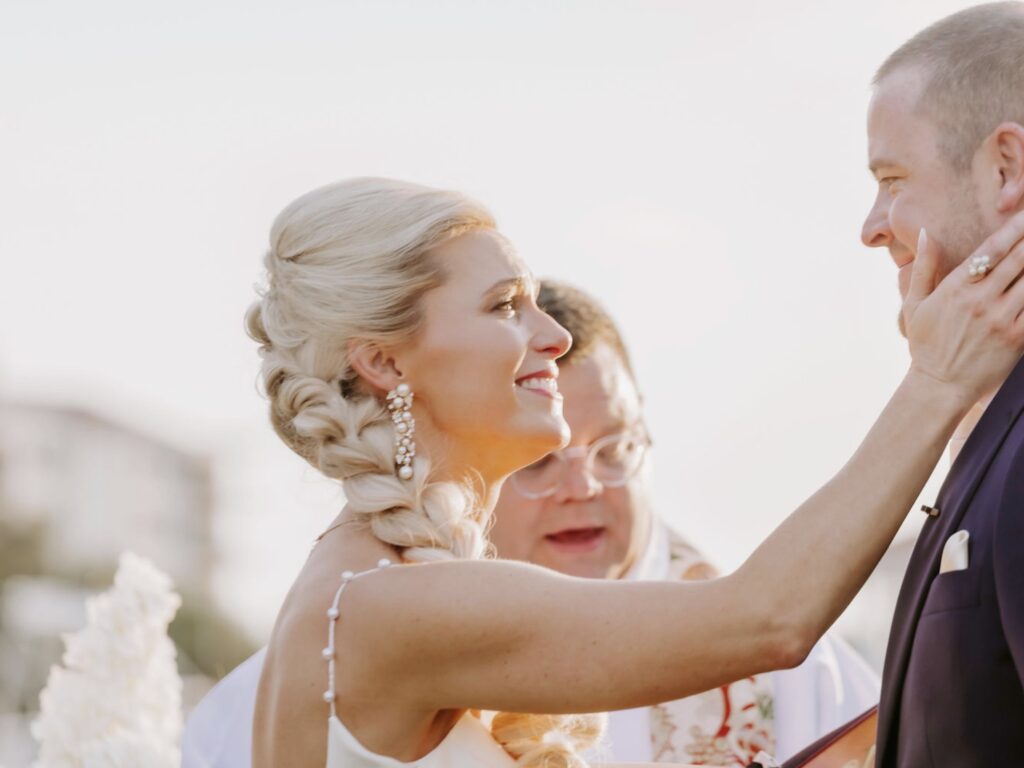 Couple at ceremony with sweet expressions and smiles at Florida wedding and gorgeous hair and makeup.  Hair is a beautiful braid.