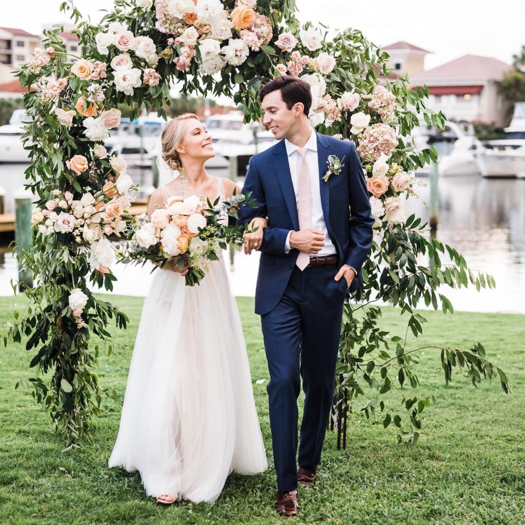 Bride with an elegant updo hairstyle in an outdoor ceremony setting with Groom with bouquet and gorgeous floral arbor - Hair and Makeup Tips for Florida Brides