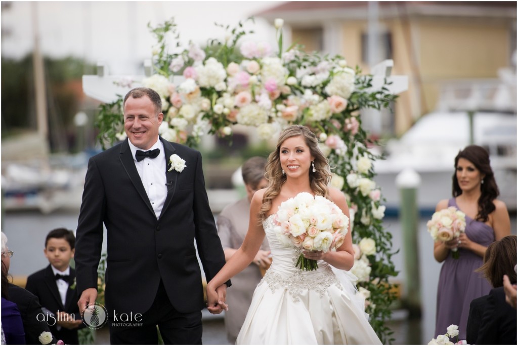 Beautiful exquisite floral arbor on the waterfront with Bride, Groom, and Maid of Honor in a May wedding at Palafox Wharf Waterfront.