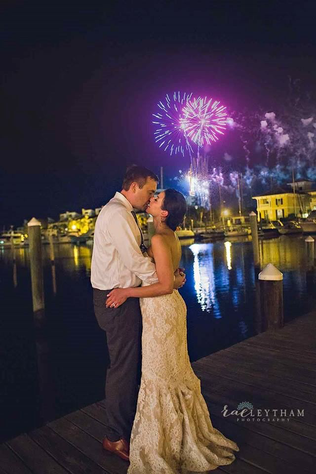 Bride and Groom embracing on dock at Palafox Wharf Waterfront with fireworks displayed in the background on the waterfront