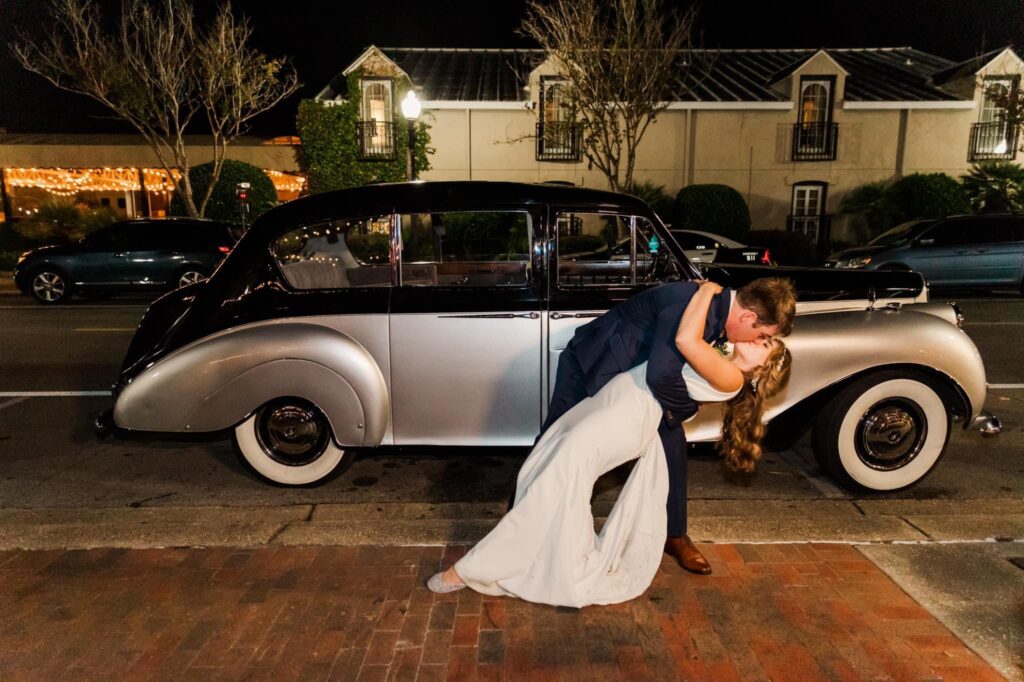 Event venue walkable for your guests in Downtown Pensacola FL near Destin.  Side view of Silver and Black Luxury Vintage Vehicle with the couple in a deep embrace in front of the vehicle.