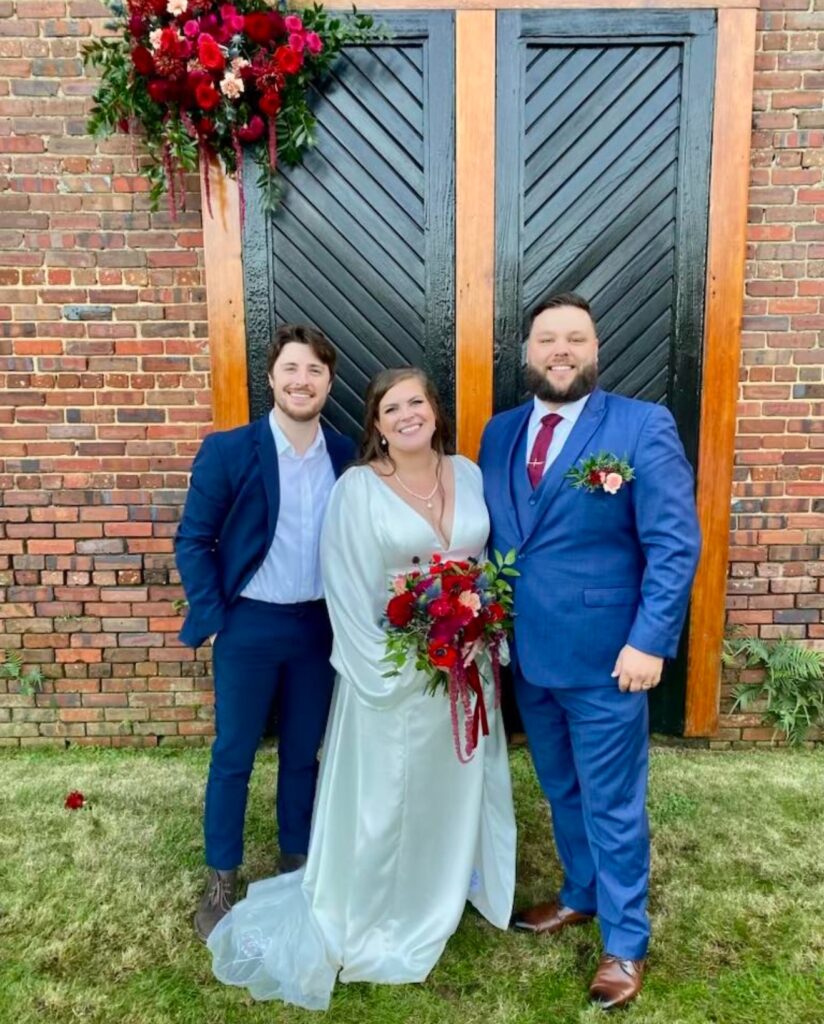 Bride and Groom along with officiant in front of black doors with florals in deep red and burgundy