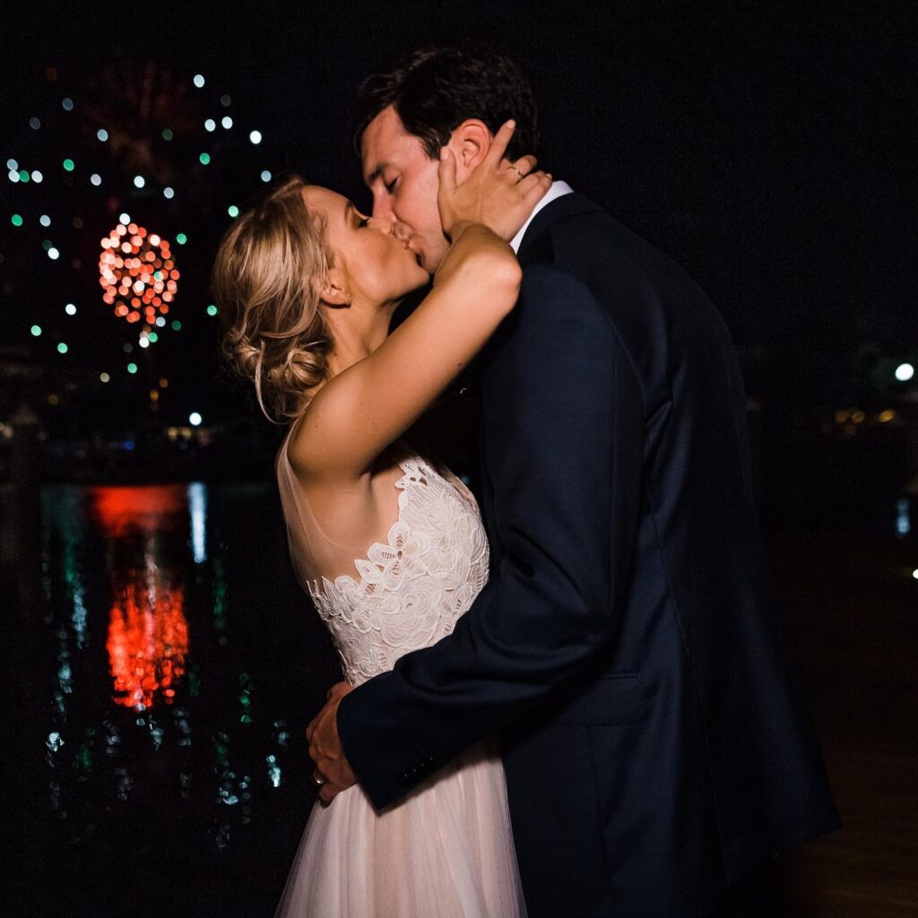 Palafox Wharf Waterfront Wedding Venue with one of their couples kissing with fireworks going off in the background and she is wearing a white lacy dress and he is in a dark suit