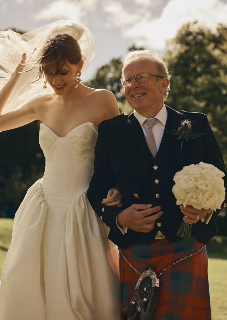 Best Pensacola Wedding Venue with dropped waist bridal dress and dad dressed in a kilt. Dad carrying bridal flowers as a breeze is blowing through the bride’s hair