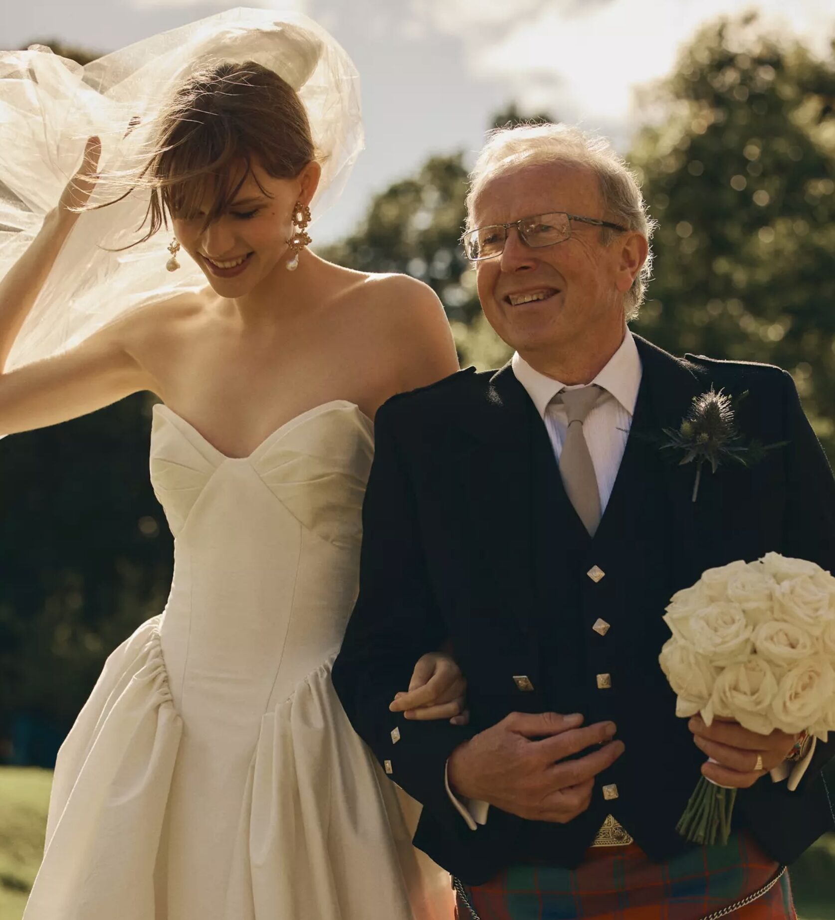 Best Pensacola Wedding Venue with dropped waist bridal dress and dad dressed in a kilt. Dad carrying bridal flowers as a breeze is blowing through the bride’s hair