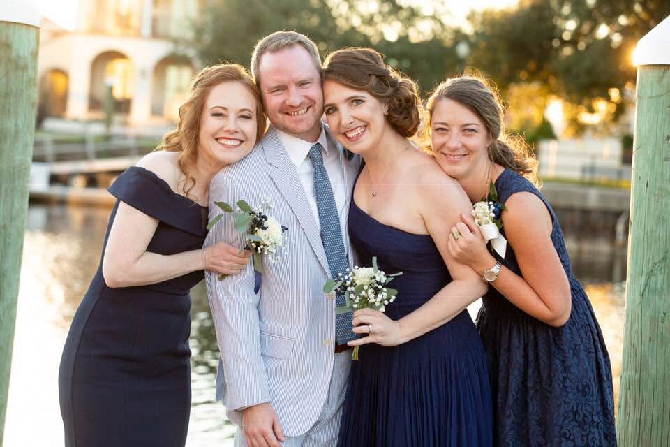 Great example of how to pose for engagement photos.  Wedding Venue called Palafox Wharf Waterfront Wedding Venue showing the Groom with Bridesmaids all smiling looking into the camera leaning against one another at the Palafox Wharf Waterfront Wedding Venue’s Dock.  Photo by Patsy Brown Photography.  How to Wedding Plan