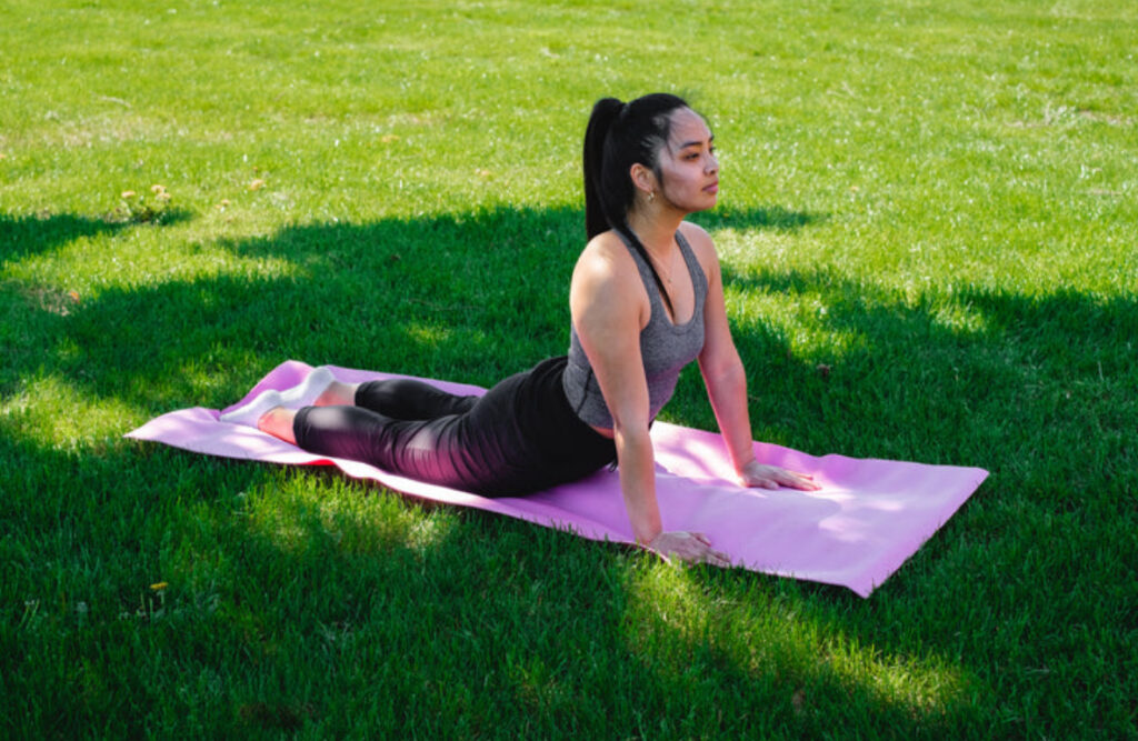 Bride on Palafox Wharf Waterfront Wedding Venue lawn practicing yoga and she is on a pink towel and dressed in gray top and black pants