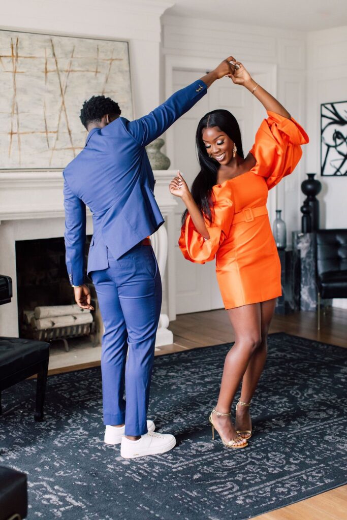 The Dance Pose here is brought to you by Palafox Wharf Waterfront Weddings and Event Venue and you can see the joy in the bride's face and he is in a blue suit and she is in a bring shine tangerine with an empire waist and large bellowing sleeves illustrating a twirl dance pose.