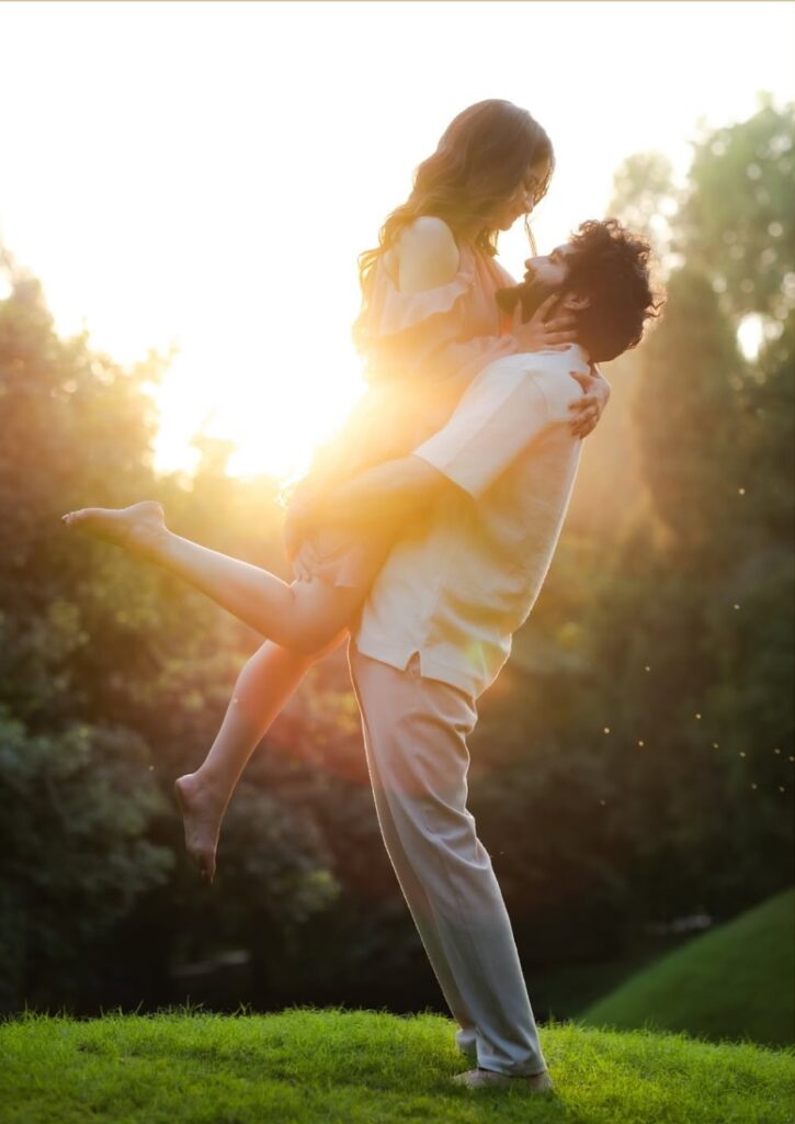 Here Palafox Wharf Waterfront Wedding Venue is illustrating a how to pose for the Life and Smile pose where the Groom is holding the Bride up off the ground in a park with both smiling together and she has here hand on his neck and the side of his face