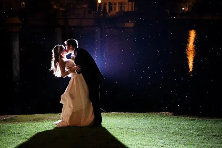 Palafox Wharf Wedding Venue on the green (lawn) with bride and groom being photographed at night  at the water's edge and a street light shining down into the water with the bride wearing a white dress and groom in a dark suit