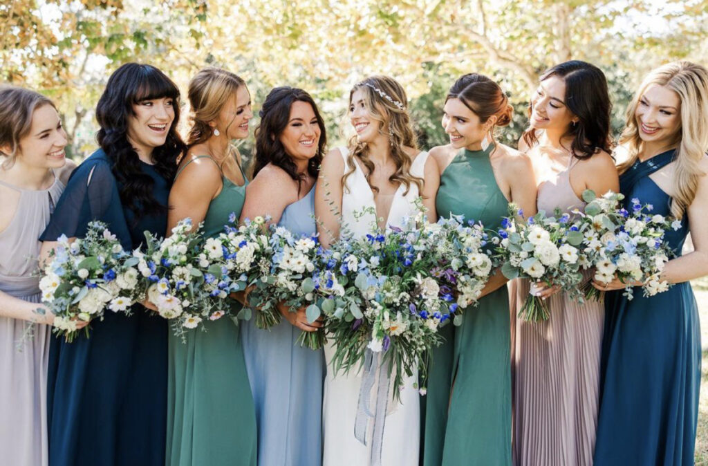 All the girls and bride together with their blue and white bouquets in mix matched dresses in blues, blush, and mauve celebrating the bride's wedding at Palafox Wharf Waterfront Wedding Venue