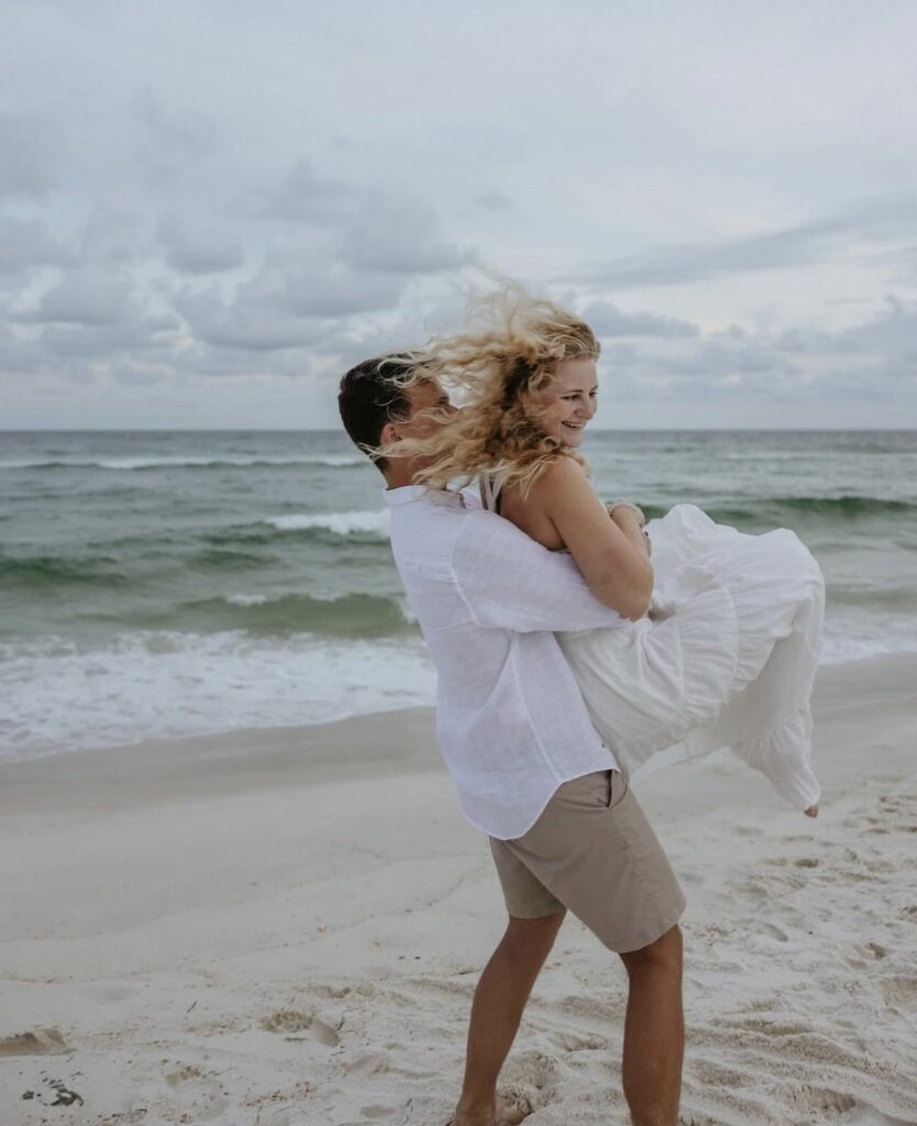 Small wedding venues in Pensacola Florida with Palafox Wharf Waterfront’s couple at the beach which is 15 minutes away from the venue and she is in a white beach dress and he is in a white shirt and brown pants