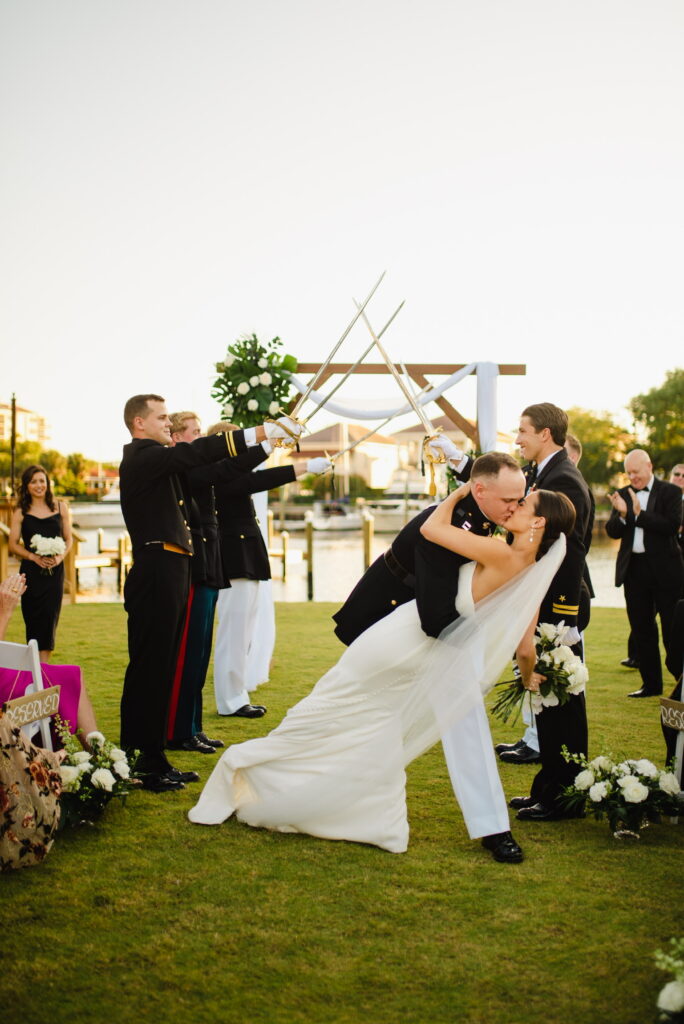 Wedding Venues Pensacola showing Destination bride and groom with sword ceremony with military on green grass on waterfront