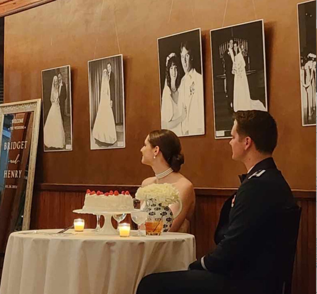 Wedding Venue Pensacola with Pensacola near Destin Wedding Venue showing unique personal black and white photos on copper wall with bride and groom seated at round table with their wedding cake being toasted by bride's mother