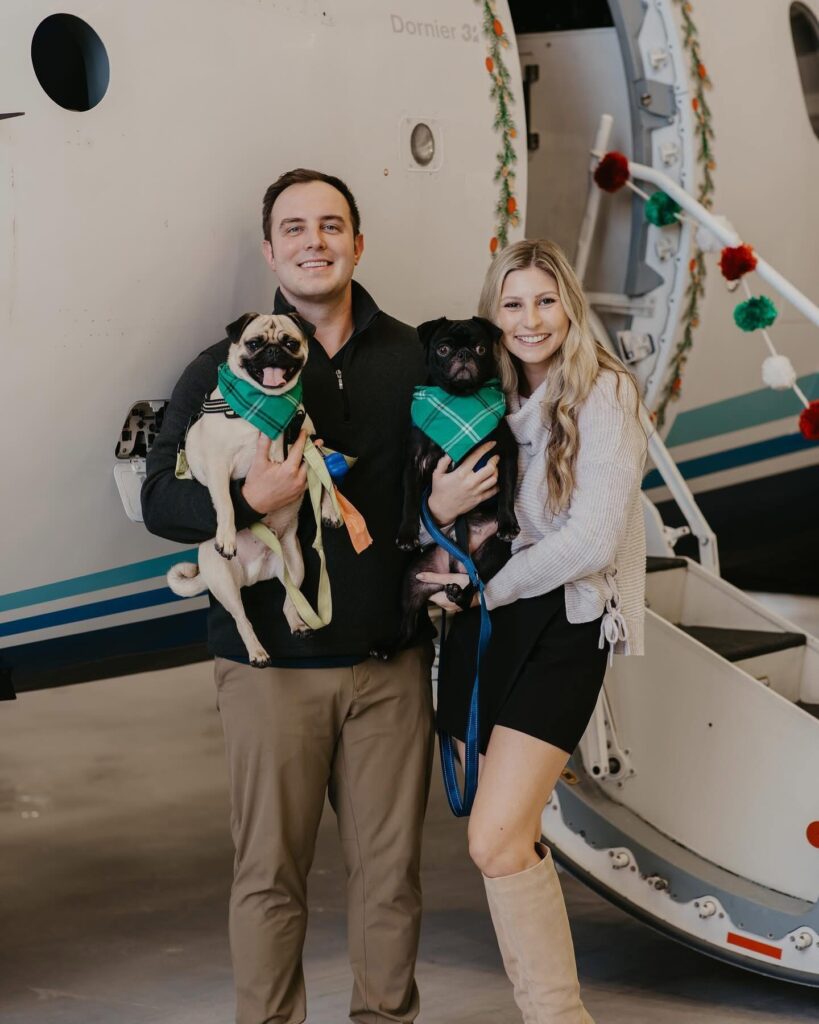 Wedding Venues Pensacola showing with a couple in front of a plane and they are holding 2 doggies in green scarves