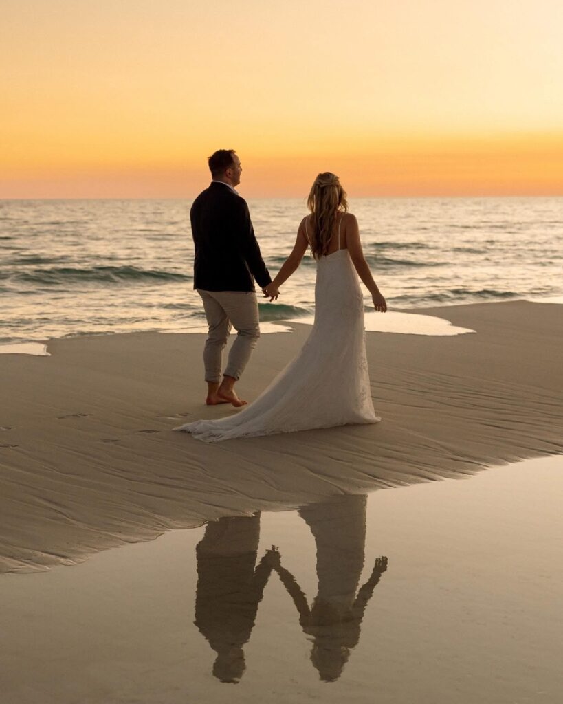 Best Wedding Dates for 2026: Perfect Days to Say “I Do” in Pensacola and here Bride and groom holding hands while walking barefoot along the beach at sunset. Bride and Groom holding their wedding day at Palafox Wharf Waterfront Pensacola Florida