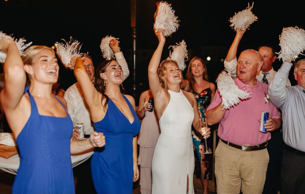 Joyful group of wedding guests on deck at Palafox Wharf waterfront doing a cheer with shakers