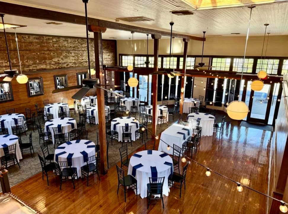 Waterfront weddings at the Palafox Wharf Waterfront Wedding Venue an event venue pensacola showing the interior with tables set up with white linens and navy blue napkins with great sun light coming through the windows and skylights