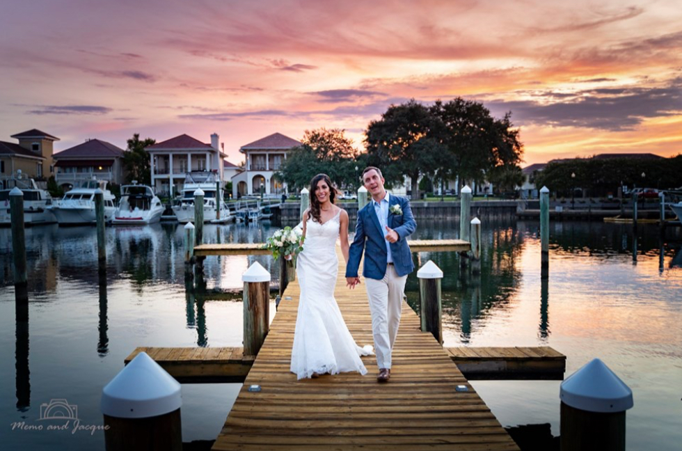 the palafox wharf waterfront wedding venue pensacola photos showing gold, pink, and orange colors for a gorgeous sunset with bride and groom on dock and she is holding her bouquet