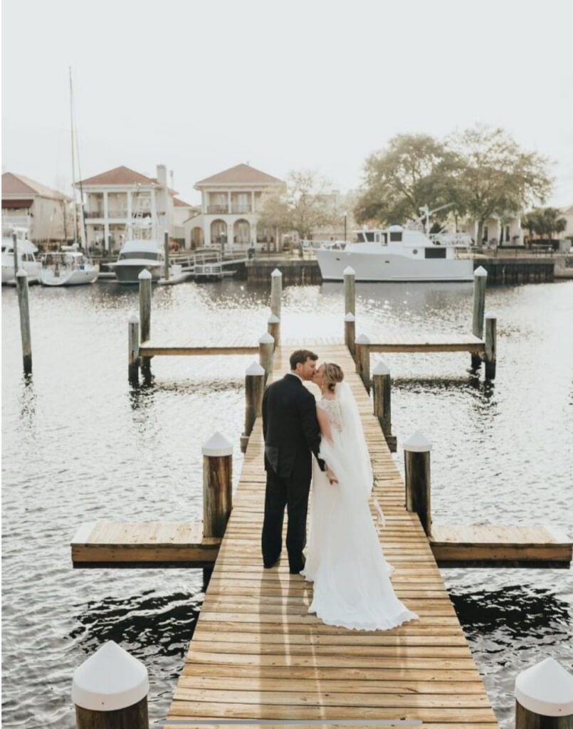 Palafox wharf waterfront wedding venue with bride and groom kissing on the docking with simmering water and boats and homes in the background