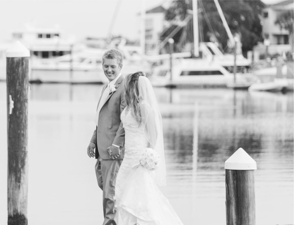 Palafox wharf waterfront wedding venue showing the owner of The Bridal Loft, a wedding and prom dress shop, in Pensacola, FL, and here with her groom walking down the dock in this black and white photo

