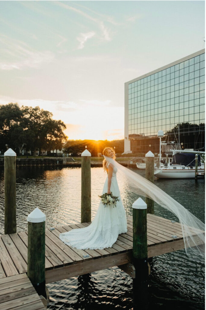 Palafox Wharf Waterfront Wedding near Destin Mobile Tallahassee showing bride in her white dress with golden hour and large building in the background along with boats
