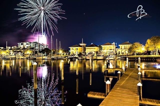 Wedding Venue Pensacola with the Wedding Day Checklist:  10 Critical Steps to Avoid Wedding Day Disasters showing Patsy Brown Photography’s great firework show viewing from palafox Wharf waterfront wedding venue with a bride and groom from Kansas and she is in white and he is in a black suit with a black vest and they are on the dock at the venue