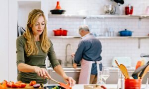 a woman prepping for cooking in a kitchen and man in background at the sink and both of them are thinking about their wedding ceremony and reception near me in Pensacola Fl at Palafox Wharf Waterfront Wedding Venue