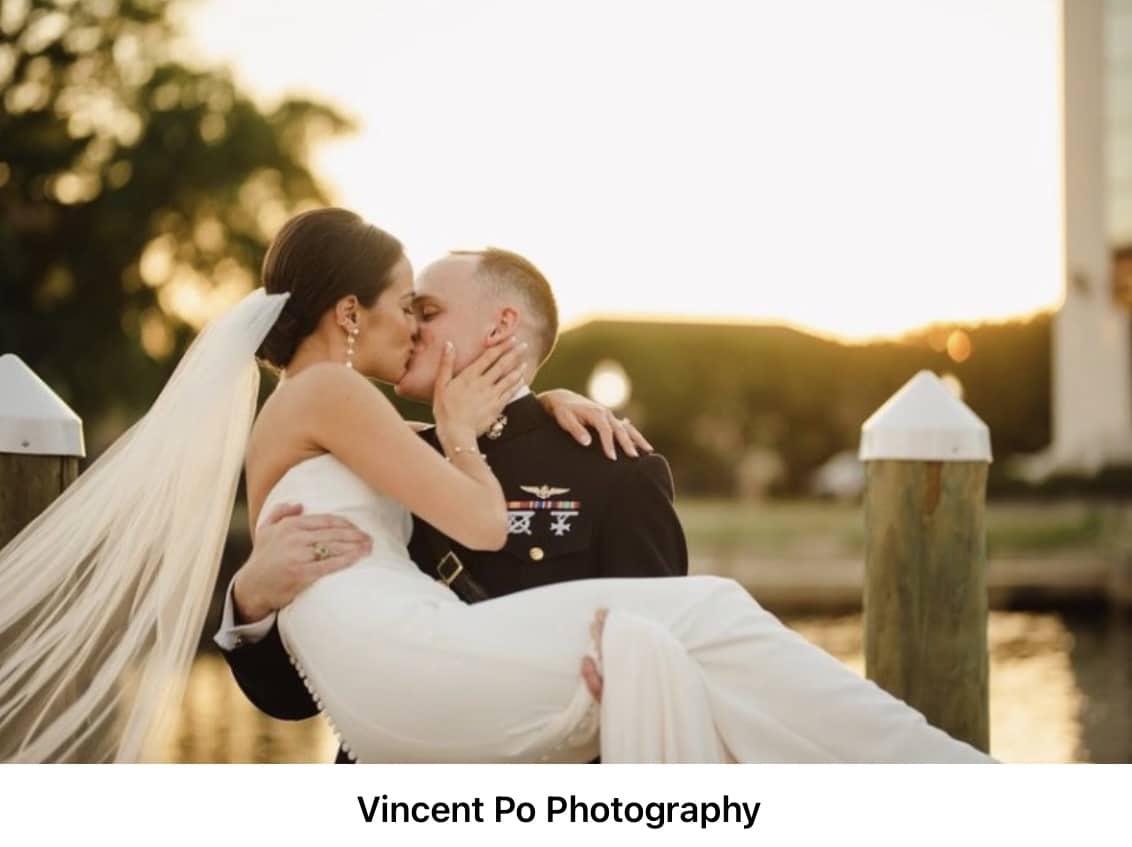 Unique waterfront wedding venues with this being palafox wharf waterfront wedding venue with military groom carrying and kissing bride in white dress during the golden hour