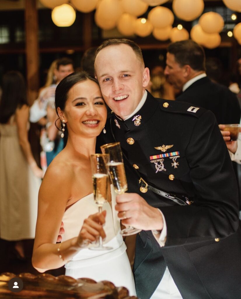 Wedding venues pensacola fl showing the interior of Palafox Wharf Waterfront Wedding Venue with a nice looking couple, she in white and he in military uniform, with champagne in their hands toasting and cafe lighting above with lanterns at the gorgeous cocktail bar