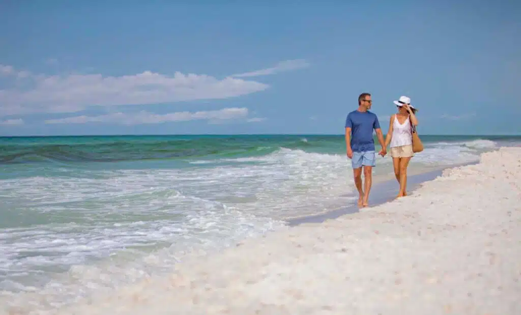 Newly engaged couple walking on the beach with white sand after touring whimsical wedding places