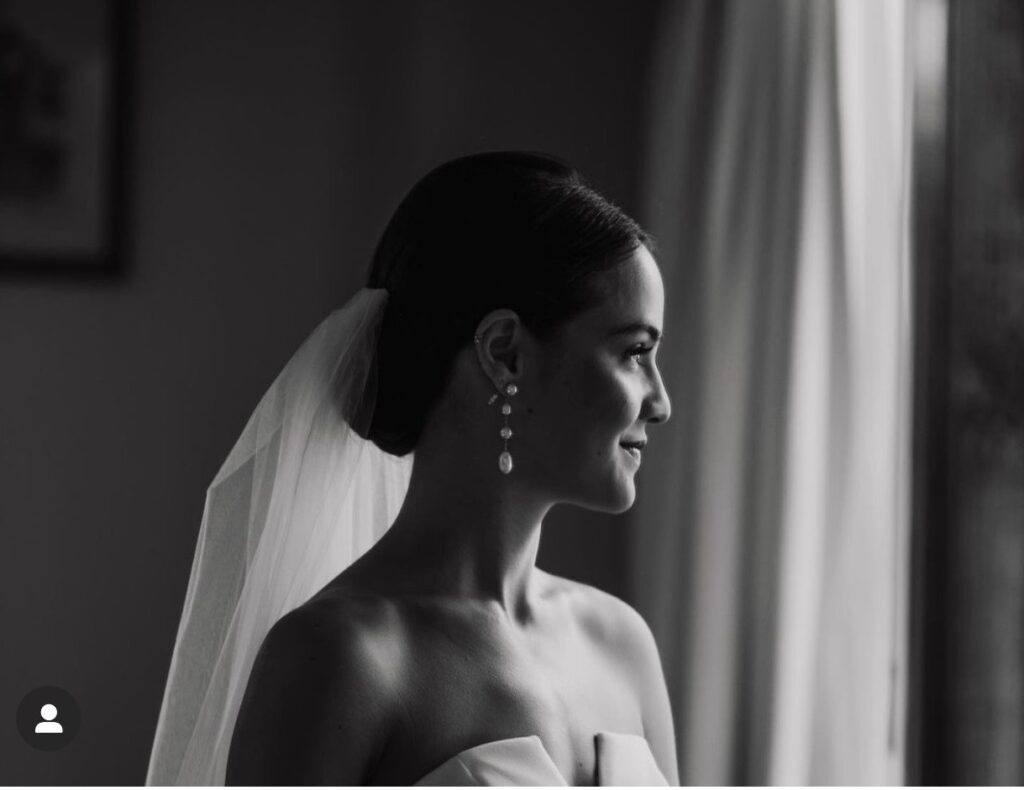 Bride in strapless wedding dress with veil smiling while gazing out window in black and white photo, featuring wedding planning introduction instructions.